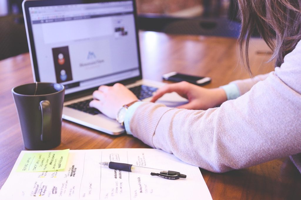 Bureau avec une tasse, une feuille de notes et un stylo ainsi qu'un ordinateur sur lequel quelqu'un est en train de taper.